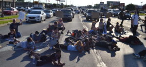 Protesters lay down on the street, blocking traffic as drivers lean out of their cars in support.