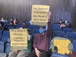 Stephen Lane holds up yellow placard at a City County Council, reading "The system is broken: We need a new one!"