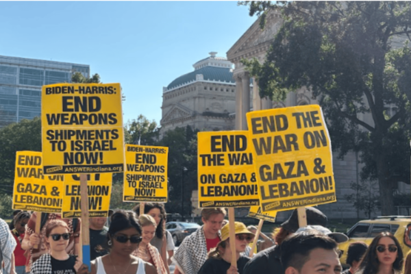 People standing in DC to protest, holding signs that read "End the War on Gaza & Lebanon"