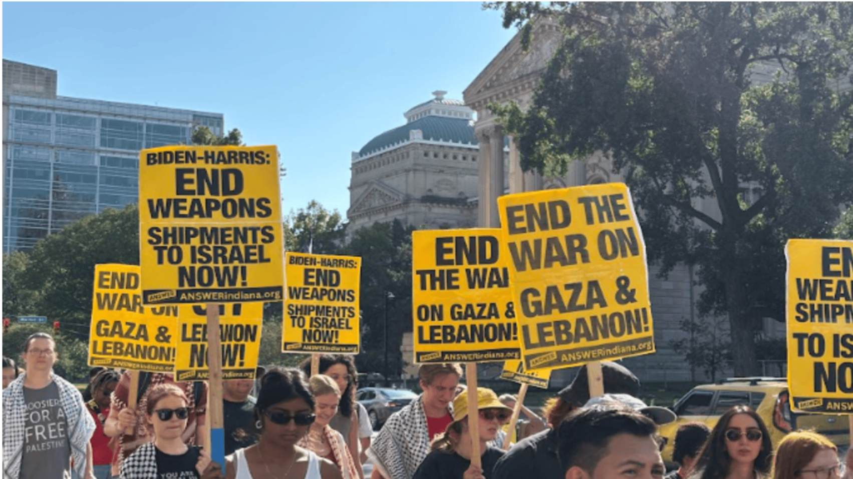 People standing in DC to protest, holding signs that read "End the War on Gaza & Lebanon"